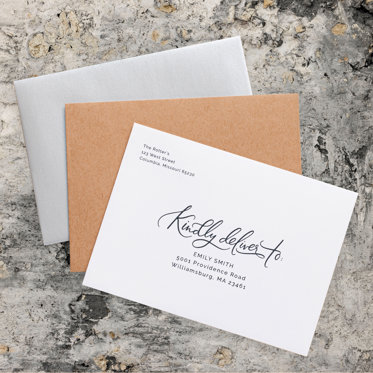 Stylish envelope addressing card with elegant script that reads 'Kindly deliver to,' paired with kraft and metallic silver envelopes on a textured stone background.