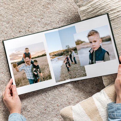 Hands holding an open photo book with a collage layout of images on the interior pages featuring photos of a family.