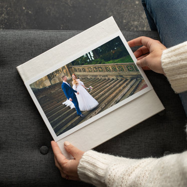 A hardcover wedding photo book with a sand linen cover and skinny dust jacket featuring a photo of a couple outside on a grand staircase on their wedding day. 