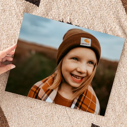 A hand holding a large photo print of a close-up picture of a child smiling.