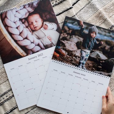 Two personalized monthly wall calendars from Mpix featuring large photos celebrating the month above a typical calendar grid. One has spiral binding on top, and the other in the middle. 