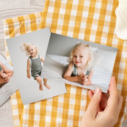 A hand spreading out several 4x6 photo prints across a table with yellow and white checkerboard placemats.