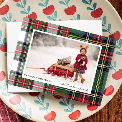 A holiday card with plaid background and a wintry photo of a young child outside in the snow.