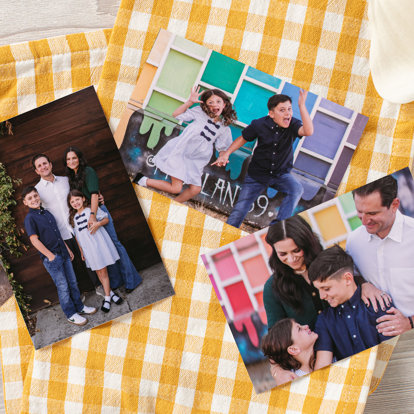 A few photo prints laid out on a counter and yellow gingham kitchen towel. The photos feature a family four doing a photo shoot in front of a colorful exterior wall.