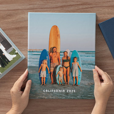 Hands holding a closed Slip-In Photo Album from Mpix showing the custom cover featuring a family photo on the beach and text that reads "California 2025"
