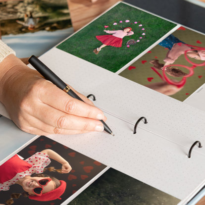 A hand flipping the page of a slip-in photo album showing the pocketed pages that contain Valentine's Day themed photos of a little girl.