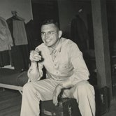 Founder Bill Miller in U.S. Army Signal Corps uniform, seated on a footlocker, smiling
