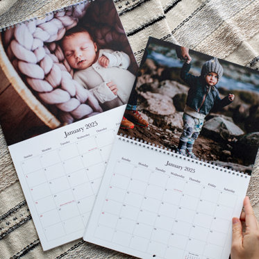 Two personalized monthly wall calendars from Mpix featuring large photos celebrating the month above a typical calendar grid. One has spiral binding on top, and the other in the middle. 