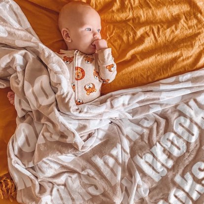 A baby covered in a name blanket.
