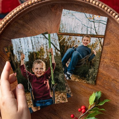 A hand holding a stack of 4x6 photo prints next to another 4x6 print laying on a wood table.