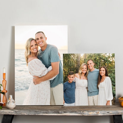 A wood print and acrylic print leaning against the wall on a side table featuring different photos of a family at the beach. 