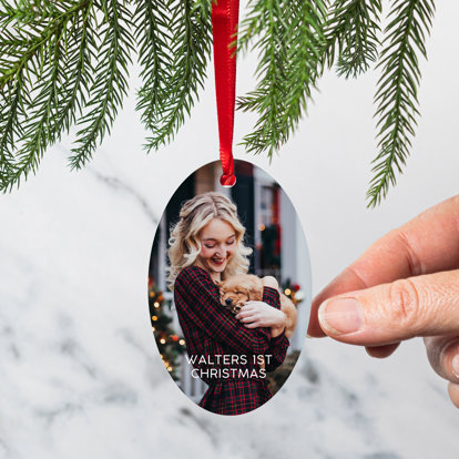 An oval shaped photo ornament with a photo of a woman holding her puppy with the text 'Walter's 1st Christmas.'