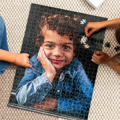 Two people assembling a photo puzzle on the floor that features a photo of a smiling boy.