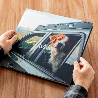 A close up of hands holding a custom hardcover photo book from Mpix featuring a photo of a pet dog on the cover with personalized text that reads "Milo"
