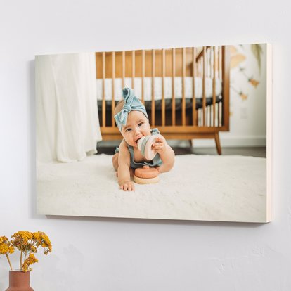 A Wooden Print of a newborn wearing a blue ribbon crawling on the floor of their room with a wooden crib in the background. 