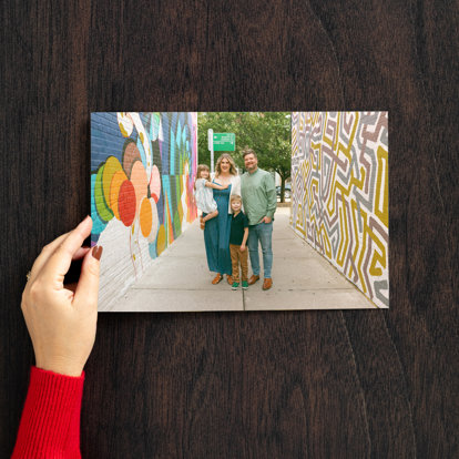 Hand holding a large horizontal print of a young family standing in an alley between two colorfully painted brick walls.