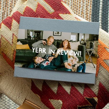 A closed photo book with a gray linen cover and photo dust jacket featuring an image of a family and personalized text that reads "YEAR IN REVIEW!" in white font.