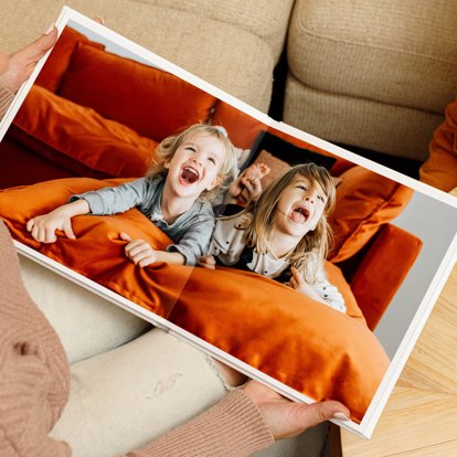 An over-the-shoulder view of a person holding an open photo book featuring an image of two young siblings playing.