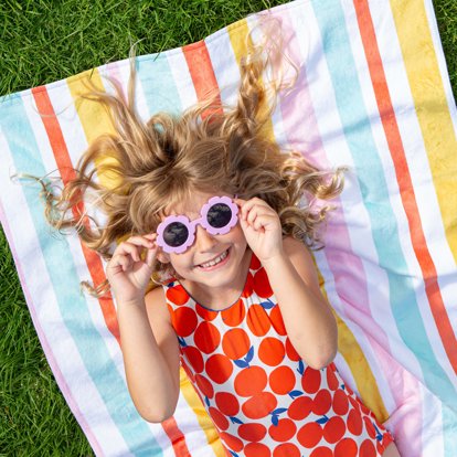A young girl laying on a personalized towel on the grass.