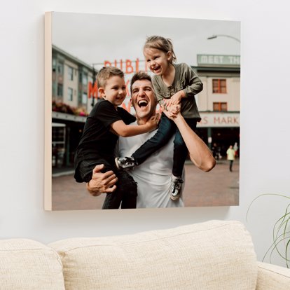 a premium wooden print of a dad holding his children in front of a public market on the wall over a couch