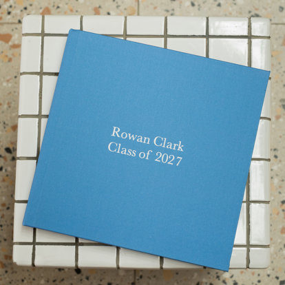 A closed photo book with a bright blue fabric cover and the title 'Rowan Clark Class of 2027'.