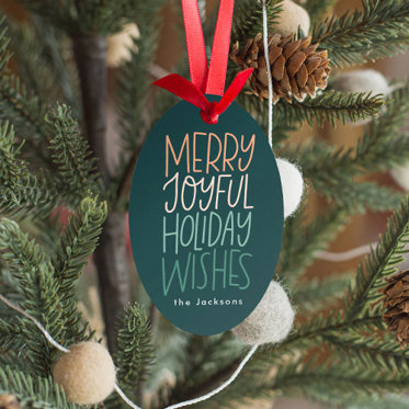 A metal ornament with a holiday design hanging with a red ribbon on a Christmas tree.