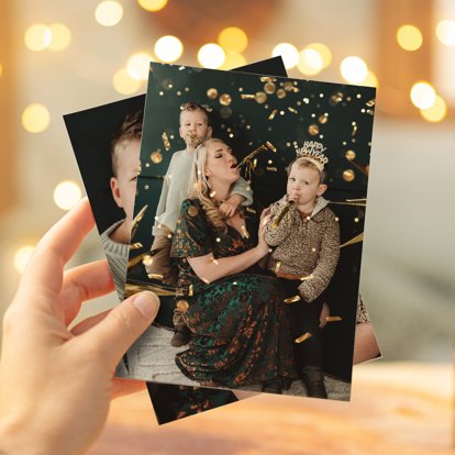 A hand holding two photo prints of a family celebrating New Year's.