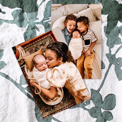 A collection of photo prints resting on a blanket decorated with plants of a young family celebrating a newborn.