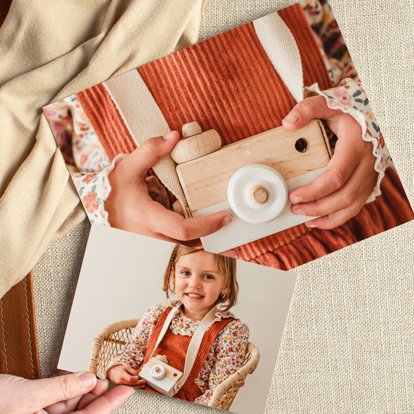 A close up of two photo prints that feature images of a young girl playing with a wooden toy camera.