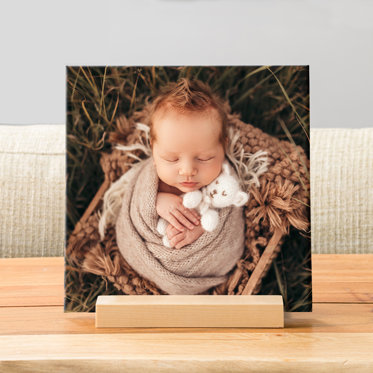 A square photo tile on a wooden display stand that features a newborn photo.