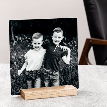 A square metal print on a wooden display stand that features a black and white photo of two young boys.