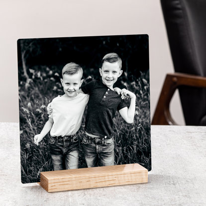 a black and white metal print of two young boys sitting comfortable in the slotted wood table stand.