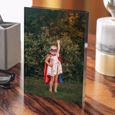 Acrylic photo block from Mpix standing on a table with a photo of a toddler in a homemade superhero costume posing in the yard. 