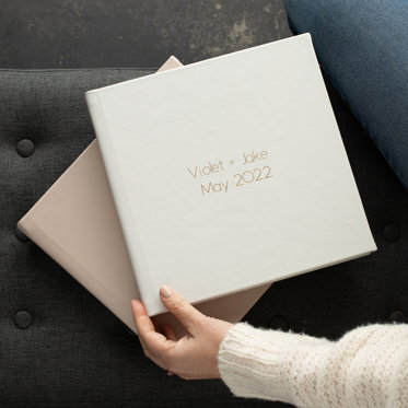 Two Signature Wedding Photo Albums from Mpix with leather covers and gold debossing resting on the couch.