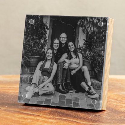 A square birch photo block from Mpix displayed on a table and featuring a black & white print of a family sitting on the front step of their home.