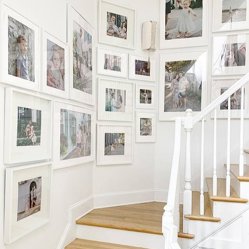 A stairway gallery wall of white-framed family photos