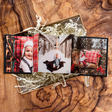 Accordion mini photo book from Mpix with a dark linen cover and christmas photos in the middle, sitting in a gift box on a wood table. 