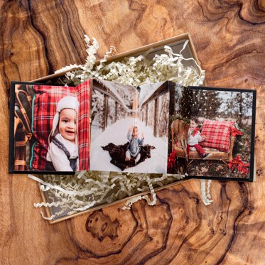 Accordion mini photo book from Mpix with a dark linen cover and christmas photos in the middle, sitting in a gift box on a wood table. 