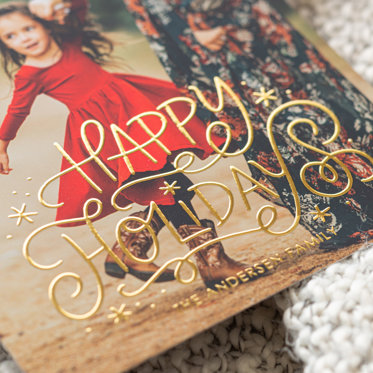 A close up of an Mpix Personalized Foil Card showing the gold foil printed on the card reading "Happy Holidays The Anderson Family"