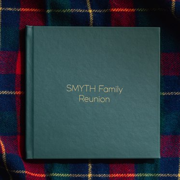 Green Leather Signature Album with gold debossing sitting on a plaid blanket. 