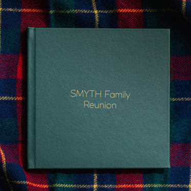 Green Leather Signature Album with gold debossing sitting on a plaid blanket. 