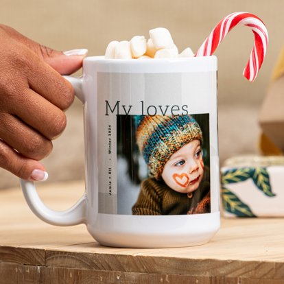 A hand holding the handle of a ceramic mug that features a design with a photo and personalized text.