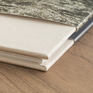 An up close view of the corner of a closed wedding photo book with a sand color linen cover and skinny dust jacket.