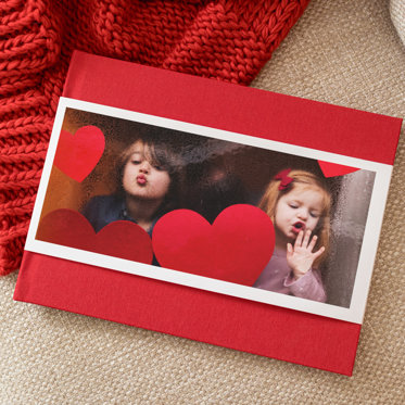 A Hardcover Photo Book from Mpix with a red linen cover and skinny dust jacket with a photo of two young girls blowing kisses