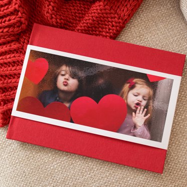 A Hardcover Photo Book from Mpix with a red linen cover and skinny dust jacket with a photo of two young girls blowing kisses