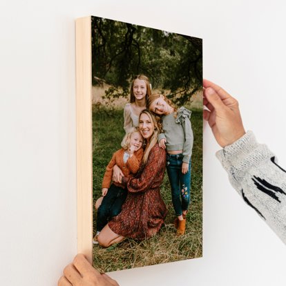 Hands hanging up a wood print of a photo of a mother with her three daughters.