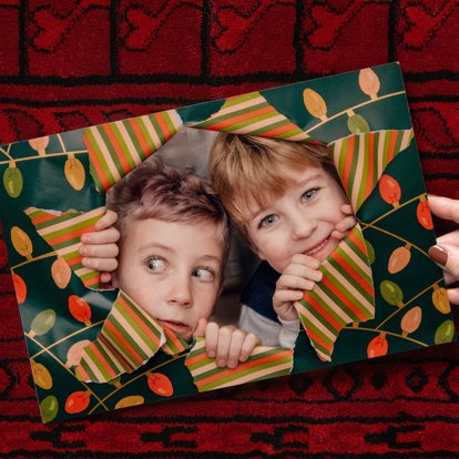 A hand holding a photo print featuring an image of children looking through a ripped hole in Christmas wrapping paper.