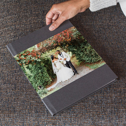 A wedding photo book with a graphite linen cover and skinny dust jacket featuring a photo of a bride and groom outside on their wedding day. 