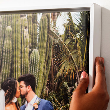 An up close view of a white float frame around a canvas print featuring a photo of a bride and groom outside kissing.