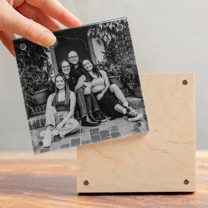 A close up of the hand of an Mpix worker assembling a birch photo block that features a black & white print of a family sitting on the front step of their home.